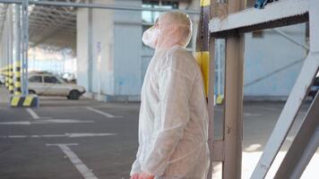 a man in a protective suit slowly sitting down in an empty parking lot video