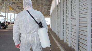 un hombre en un protector traje y máscara con un agua pulverización herramienta caminando en un vacío estacionamiento lote video