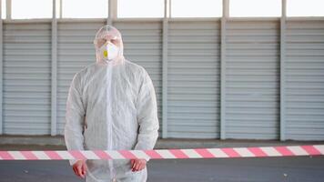 a person in a white protective suit and mask showing people to not pass the red line video