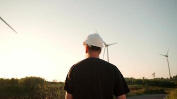 een Mens in een moeilijk hoed staand in voorkant van een wind turbine buitenshuis video