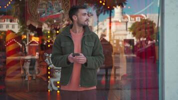 a man in a green jacket is standing in front of a carousel is looking at his phone then to the camera video