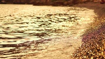 Abstract sea summer ocean sunset nature background. Small waves on golden water surface in motion blur with golden bokeh lights from sun. Holiday, vacation and recreational concept. Nobody Slow motion video