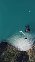 vertical aéreo Visão em calma azul mar e vulcânico rochoso margens. pequeno ondas em água superfície dentro movimento borrão. natureza verão oceano mar de praia fundo. ninguém. feriado, período de férias e viagem conceito video