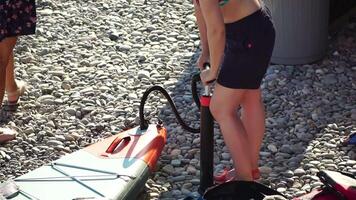 vrouw blaast op sta op plas bord. persoon pompen Aan strand dichtbij omhoog schot van pomp en persoon handen in focus terwijl constant pompen. langzaam beweging video