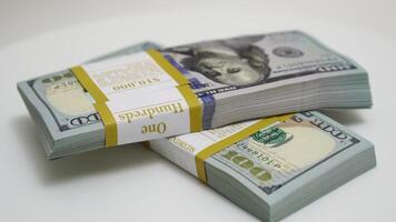 stack of bank bundles with US dollars on a white background. Close-up shot of new, freshly printed hundred-dollar bills rotating on a table. cash flow, business investment, or big money concepts. video