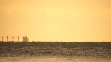 Mirage of cargo ship in the sea beyond the horizon. Ship sailing in the sea. Small waves on the golden surface of warm water with bokeh lights from the sun. Sea, nature and outdoor travel. video