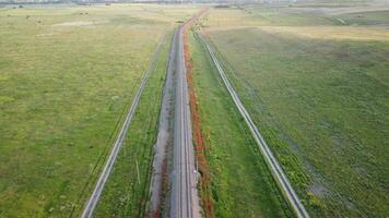 aerial view of a railroad track cutting through a lush field of green wheat in countryside. Field of wheat blowing in the wind like green sea. Agronomy, industry and food production. video