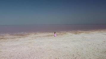 Woman in flying dress on pink salt lake. Salt production facilities saline evaporation pond fields in the salty lake. video