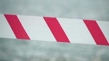 Red white warning tape barrier ribbon swinging in the wind across exotic sea beach background without people. No entry Red White caution tape. No holiday concept, delayed travel, no summer plans video