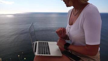 digital nómada, negocio mujer trabajando en ordenador portátil por el mar. bonito dama mecanografía en computadora por el mar a atardecer, hace un negocio transacción en línea desde un distancia. Lanza libre, remoto trabajo en vacaciones video