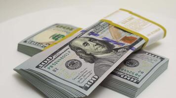 stack of bank bundles with US dollars on a white background. Close-up shot of new, freshly printed hundred-dollar bills rotating on a table. cash flow, business investment, or big money concepts. video