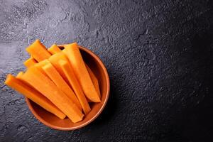 Carrot pieces on a dark background inside a bowl. photo
