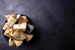 Pieces of eggplant inside a bowl on a very dark background. photo