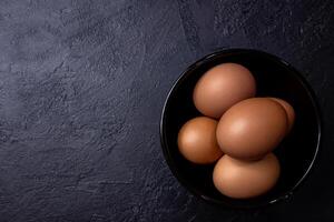 Fresh eggs in a bowl on a dark colored table. photo