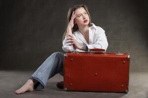 Beautiful girl sits with a vintage suitcase on a gray background. photo