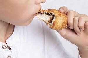 The child's hands hold a bitten croissant. There are baked goods. photo