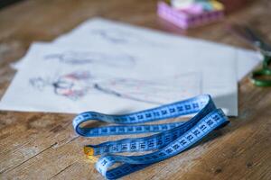 Blue measuring tape. Tailor s sketches, design work. Draft with beautiful dresses on table. Tailor concept. Close-up. photo