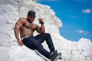 Shirtless muscular man sitting and tanning on summer sun. Outdoor sportive man with naked muscular torso. photo