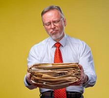 A businessman carrying pile of paperwork, over yellow background. Sad expression. to do a lot photo