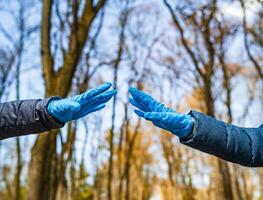 Man and female hands in medical gloves stretch to each other. Park with high trees blurred background. Selective focus. Coronovirus epidemic. COVID-19 and coronavirus identification. Pandemic photo