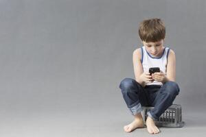 niño con un móvil teléfono. colegial mira dentro el teléfono inteligente en un gris antecedentes foto