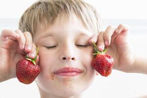 un niño con fresas el chico sostiene dos rojo bayas foto