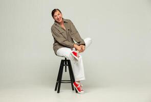 Middle-aged woman in casual clothes and red sneakers poses with a smile in the studio on a gray background photo