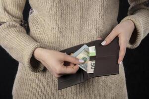 In female hands, a brown wallet with euros and dollars. photo
