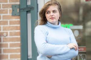 On the street, a happy blonde girl in a blue knitted sweater. photo