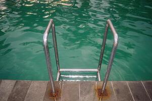 a stainless steel swimming ladder in a swimming pool with turquoise water photo