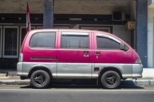 un antiguo rojo coche estacionado en el lado de un urbano carretera, Indonesia, 17 septiembre 2023. foto