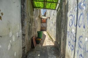 en un estrecho callejón líder a un del residente casa, usted lata ver dos grande y pequeño basura latas y además pintada en el paredes, Indonesia, 17 septiembre 2023 foto