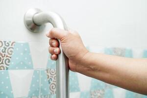 Asian woman patient use toilet support rail in bathroom, handrail safety grab bar, security in nursing hospital. photo