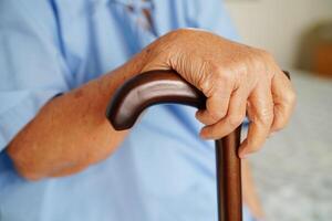 Asian elderly disability woman patient holding walking stick in wrinkled hand at hospital. photo