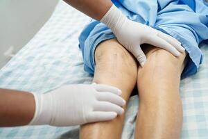 Doctor checking Asian elderly woman patient with scar knee replacement surgery in hospital. photo