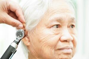 Otolaryngologist or ENT physician doctor examining senior patient ear with otoscope, hearing loss problem. photo