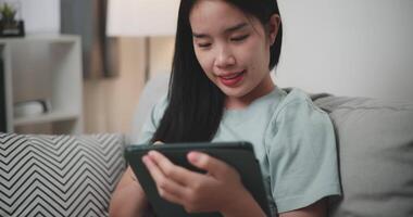 Footage selective focus shot, Happy young woman sitting on sofa using digital tablet for online shopping cashless in living room at home, Technology money wallet and Online payment concept video