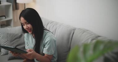 Aufnahmen Dolly und hoch Winkel Aussicht Schuss, glücklich jung Frau Sitzung auf Sofa mit Digital Tablette zum online Einkaufen bargeldlos im Leben Zimmer beim heim, Technologie Geld Brieftasche und online Zahlung Konzept video