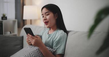 Footage selective focus shot, Happy young woman sitting on sofa holding coffee mug and enjoy using mobile phone while shopping online cashless in living room at home video