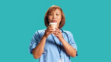 BIPOC nurse tasting instant coffee while at work, surprised by unexpected aroma. Close up shot of hospital employee drinking hot beverage with unusual aftertaste, isolated over studio background photo