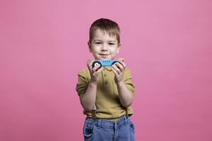 pequeño linda niño jugando alrededor el estudio con un azul auto, teniendo divertido y recreando en frente de cámara. alegre sonriente pequeño chico participación un el plastico vehículo a jugar y disfrutar ocio actividad. foto