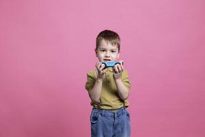 pequeño preescolar jugando alrededor el estudio con un azul vehículo, teniendo divertido y riendo en frente de cámara. alegre sonriente joven niño participación un el plastico automóvil a jugar y disfrutar actividad. foto