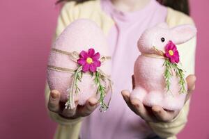 Cute small kid presenting her handmade decorated ornaments, adorable pink egg and a stuffed rabbit in studio. Little girl smiling and feeling excited about easter celebration event. Close up. photo