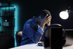 Side-view of an upset millennial woman sitting in front of laptop feeling upset, holding her head in her hands, going through stress. Female student feeling worn out, depressed, and having headache. photo