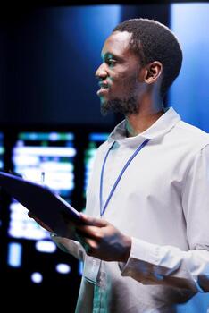 Engineer using clipboard to write down findings after monitoring energy consumption across server parts. Specialist ensuring data center sensors for temperature and humidity are in optimal condition photo