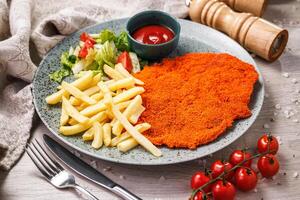 schnitzel, french fries with tomato sauce and salad on a wooden background. photo