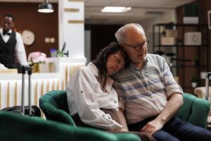 imagen exhibiendo mayor Pareja descansando en cada otro espalda en el lujoso salón área. mayor masculino y hembra clientes dormido en acogedor sofá, esperando para reservado alojamiento. foto