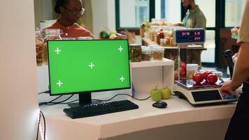 Vendor at checkout uses greenscreen on computer, showing isolated chromakey display on desktop monitor. Young adult small business owner advertises sustainable lifestyle with blank mockup. photo