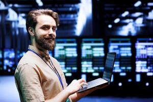 Portrait of smiling serviceman doing routine maintenance in blockchain technology application specific integrated circuit server room. Proud specialist working in crypto mining farm photo