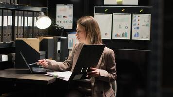 Determinated female detective inspector conducts investigation with laptop in office space. Police officer utilizing technology in incident room for forensic analysis and reviewing evidence files. photo